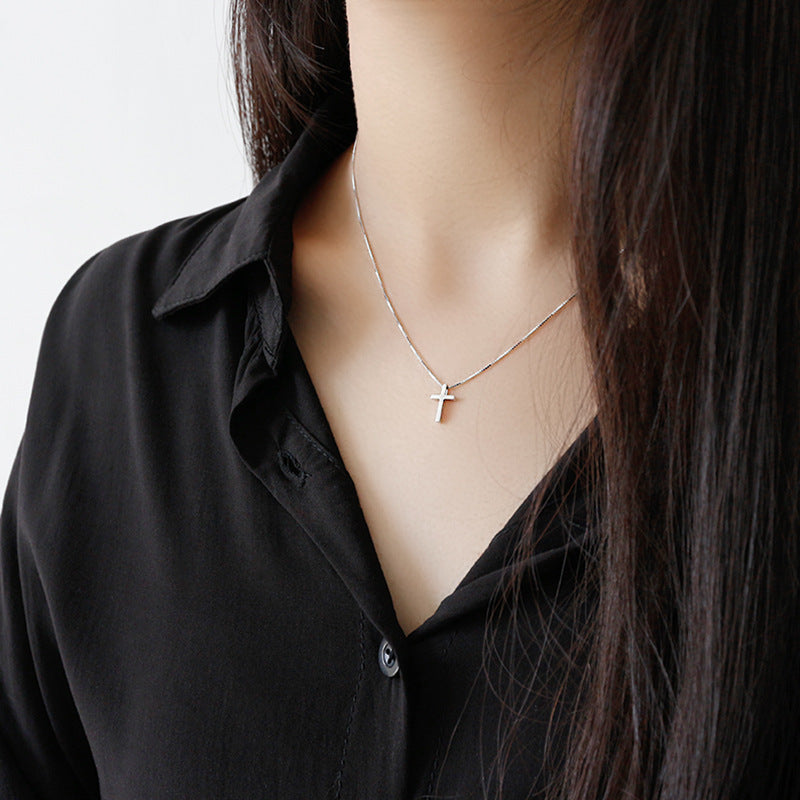 Person wearing a black shirt with a necklace featuring a cross pendant.