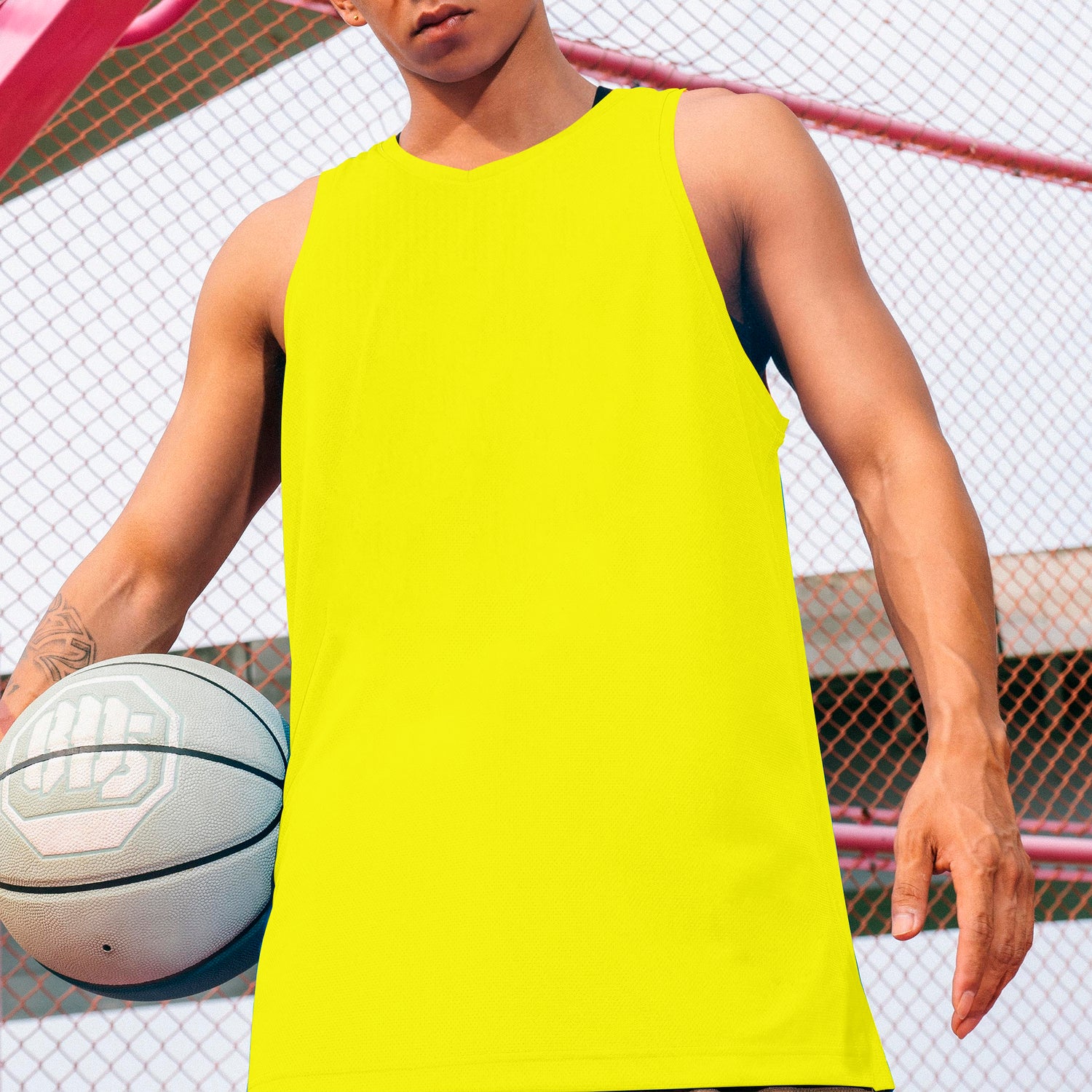 Person wearing a bright yellow tank top holding a basketball on an outdoor court.