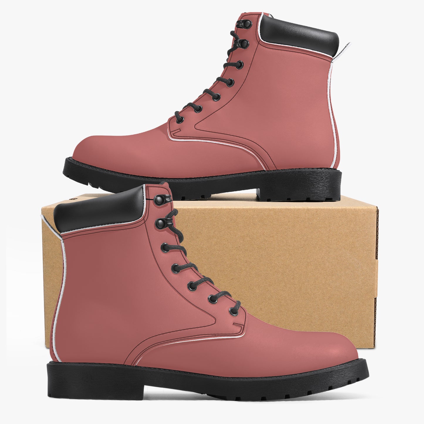 Pair of pink boots with black soles on a cardboard box against a white background