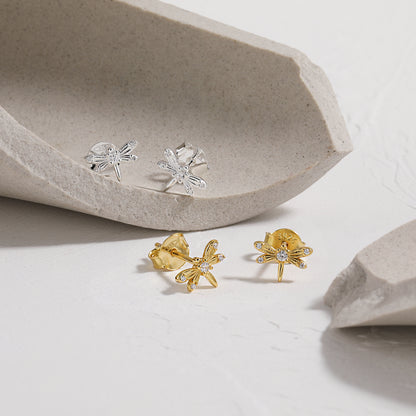 Gold and silver dragonfly earrings on a light gray surface with a stone-like background