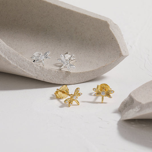 Gold and silver dragonfly earrings on a light gray surface with a stone-like background