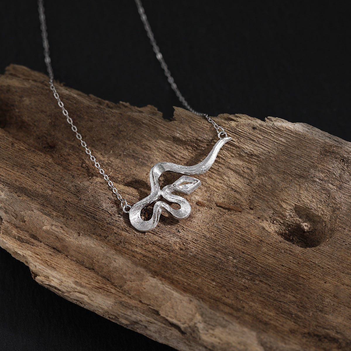 Modern Rhombus CZ curved snake pendant necklace in 925 sterling silver with cubic zirconia stone, Displayed on Wood